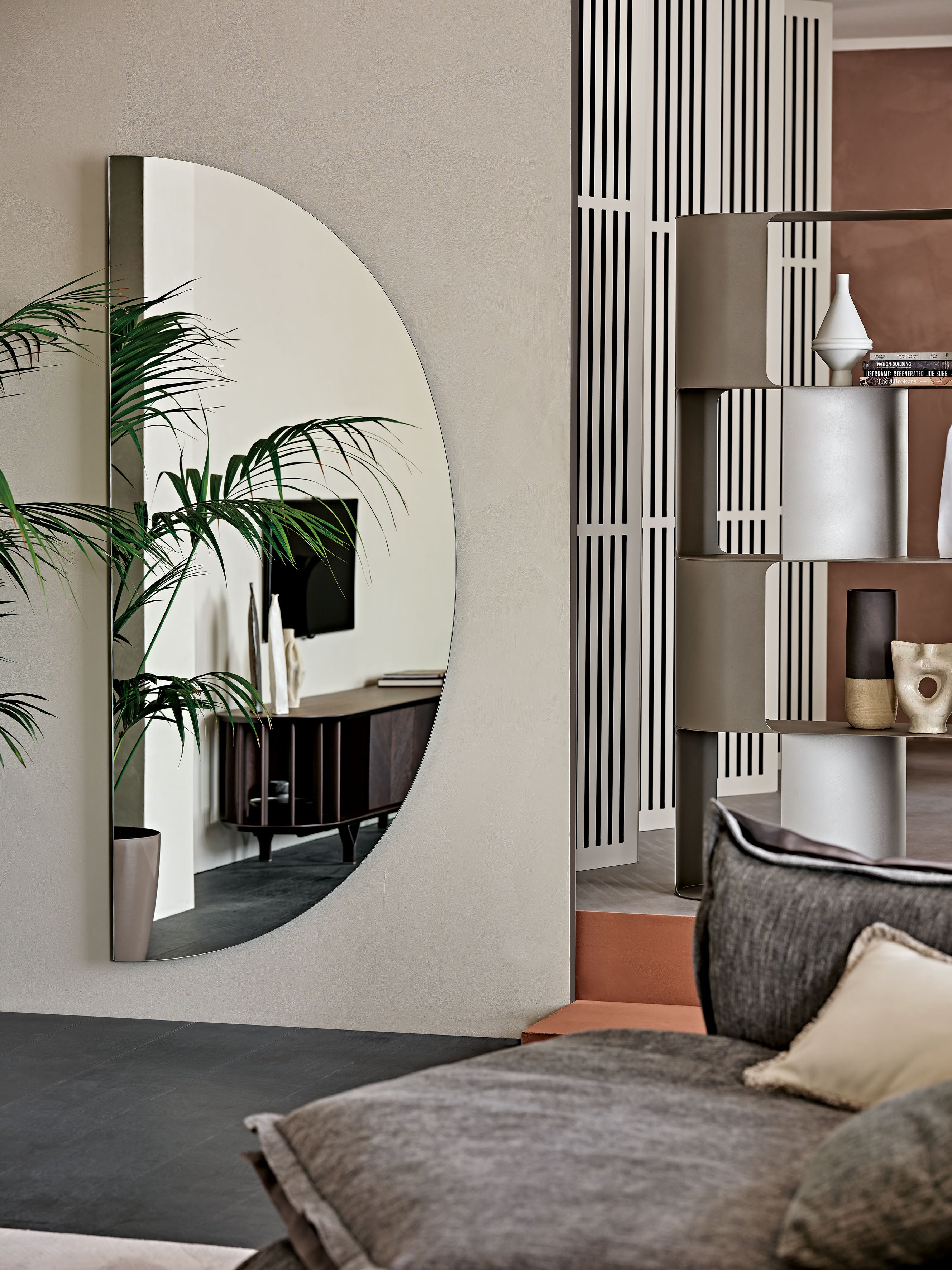 Day mirror hung vertically on a warm beige wall next to a palm
