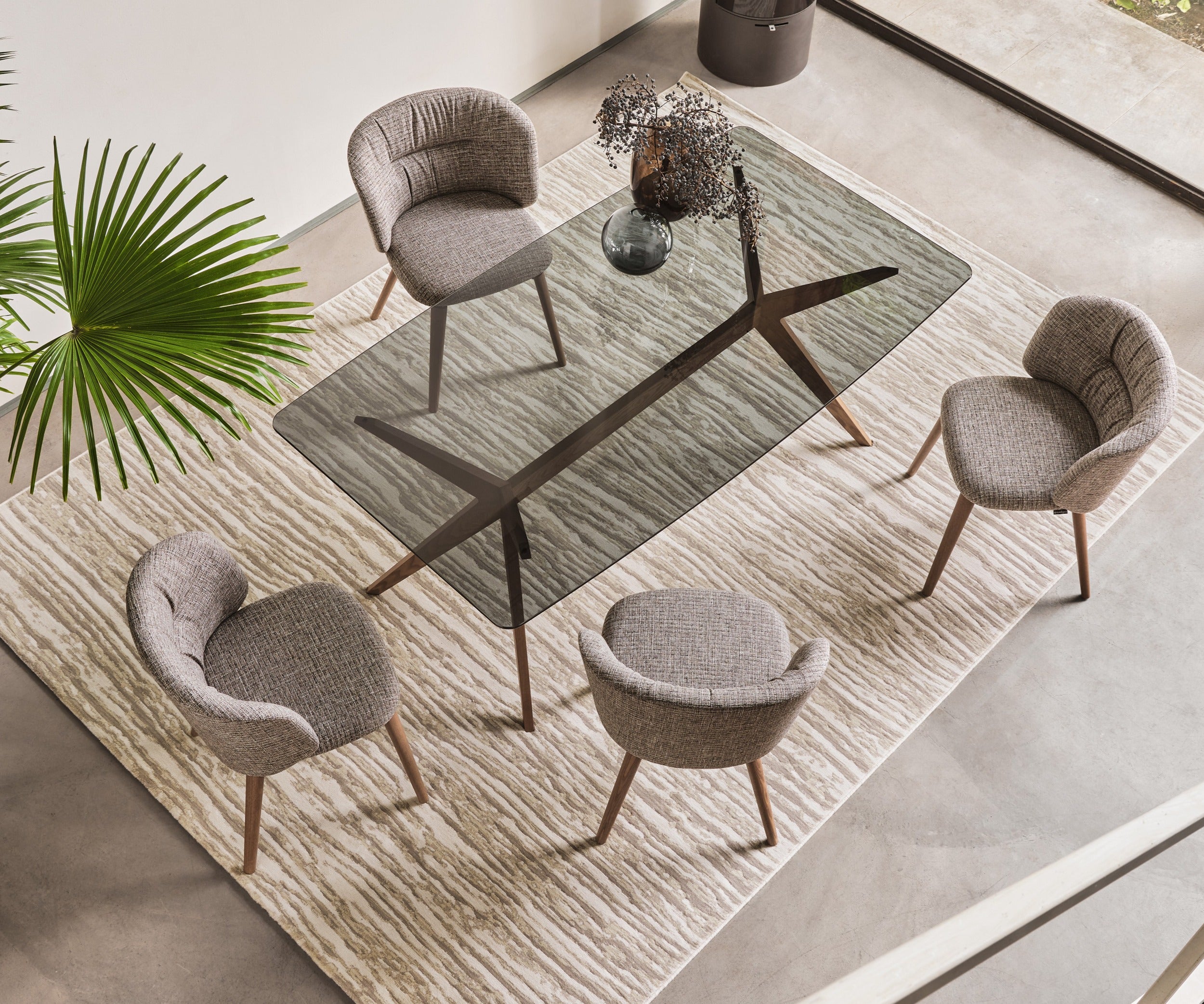 Domus rug by Calligaris under a glass dining table with four upholstered chairs, overhead view