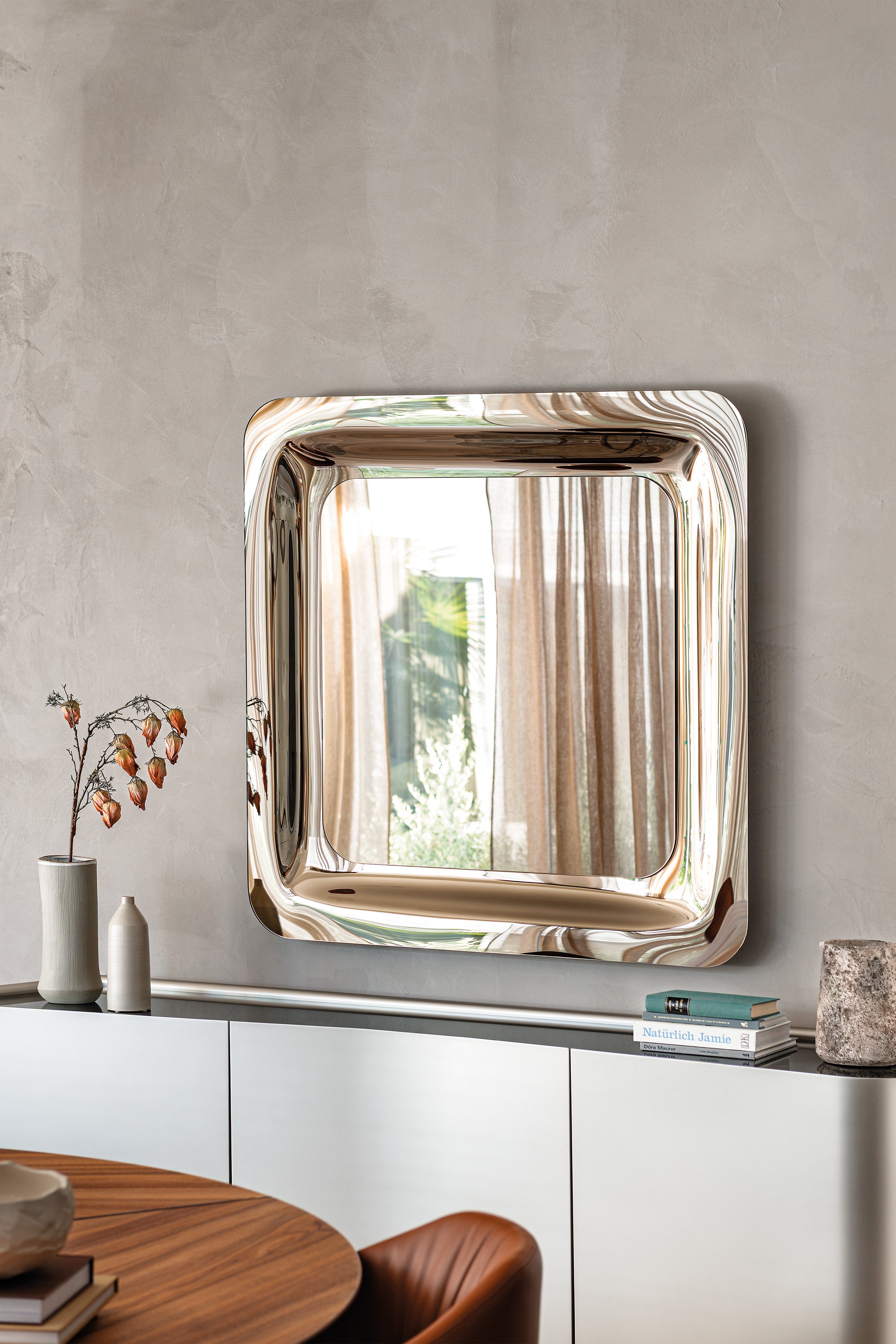 Bronze mirrored square Glenn mirror on a grey plaster wall above a white sideboard