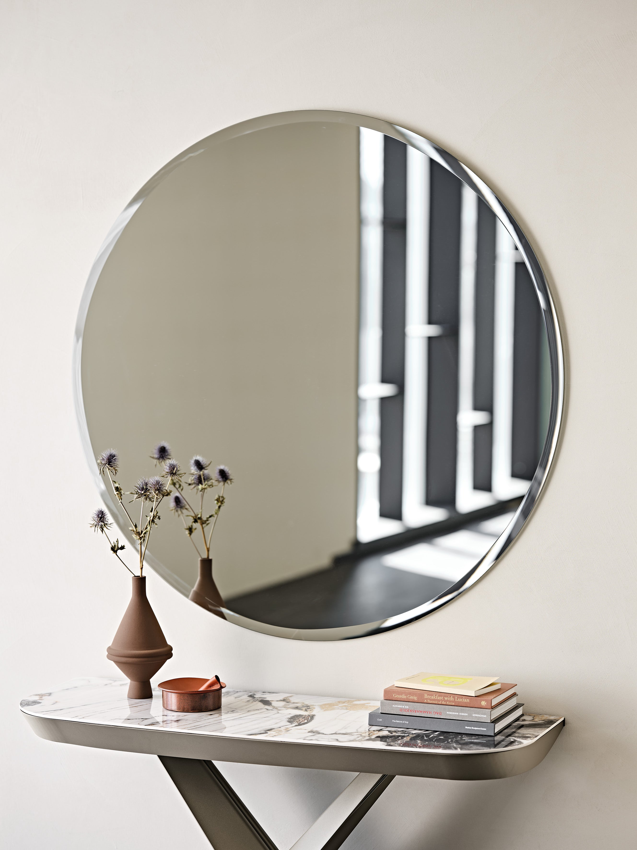 Hawaii Round mirror above a marble-top console with a terracotta vase