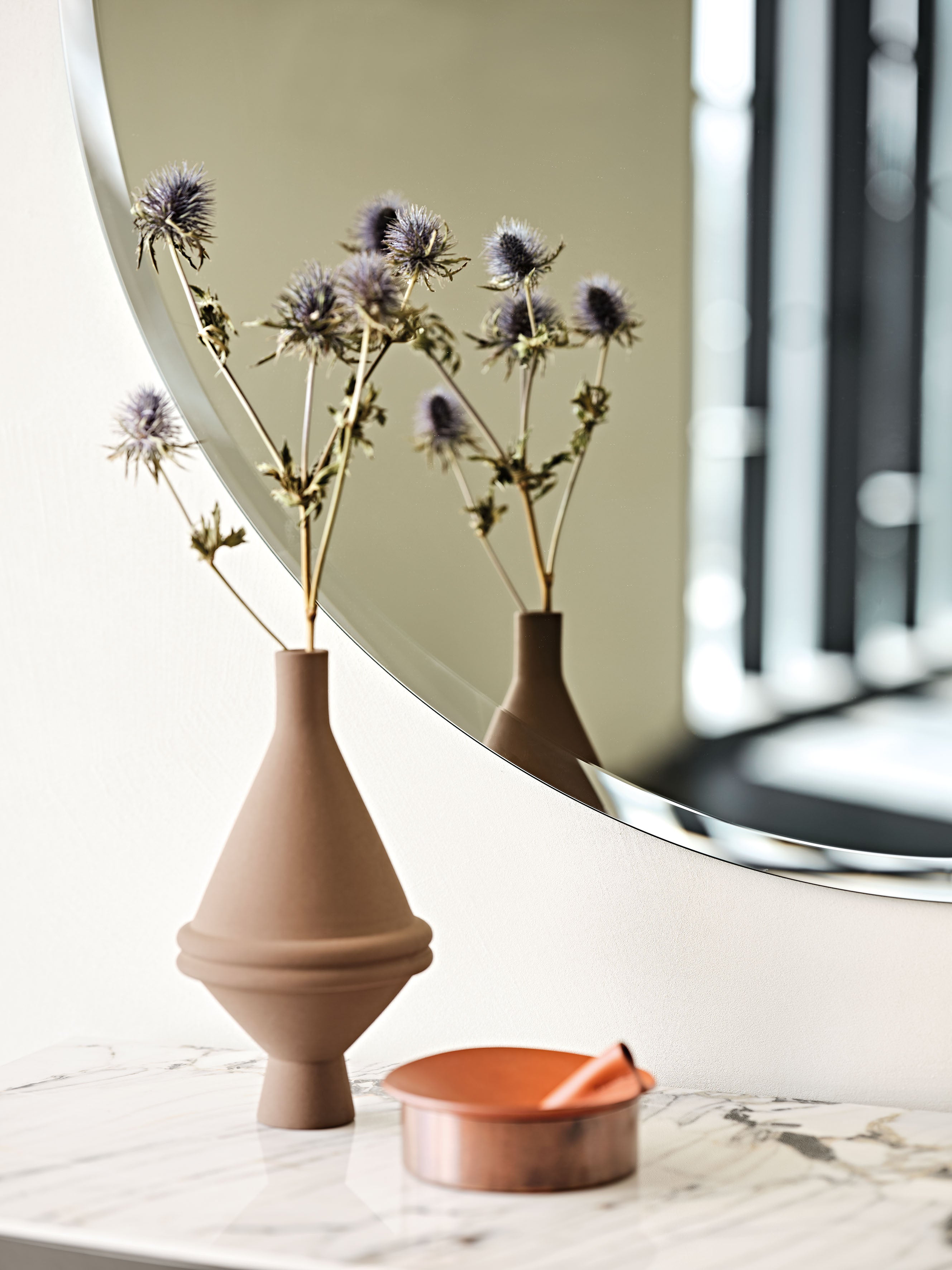 Close-up of the Hawaii Round mirror's bevelled rim, with a terracotta vase