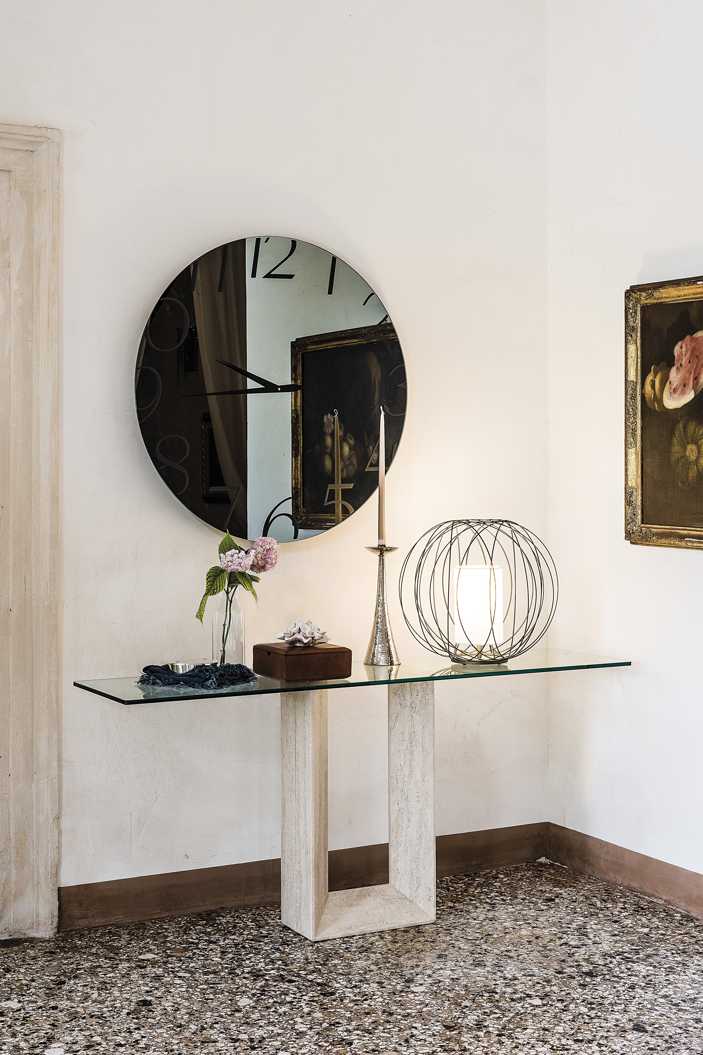 Moment mirror: round fumé Moment above a glass-top console with stone legs in a white room