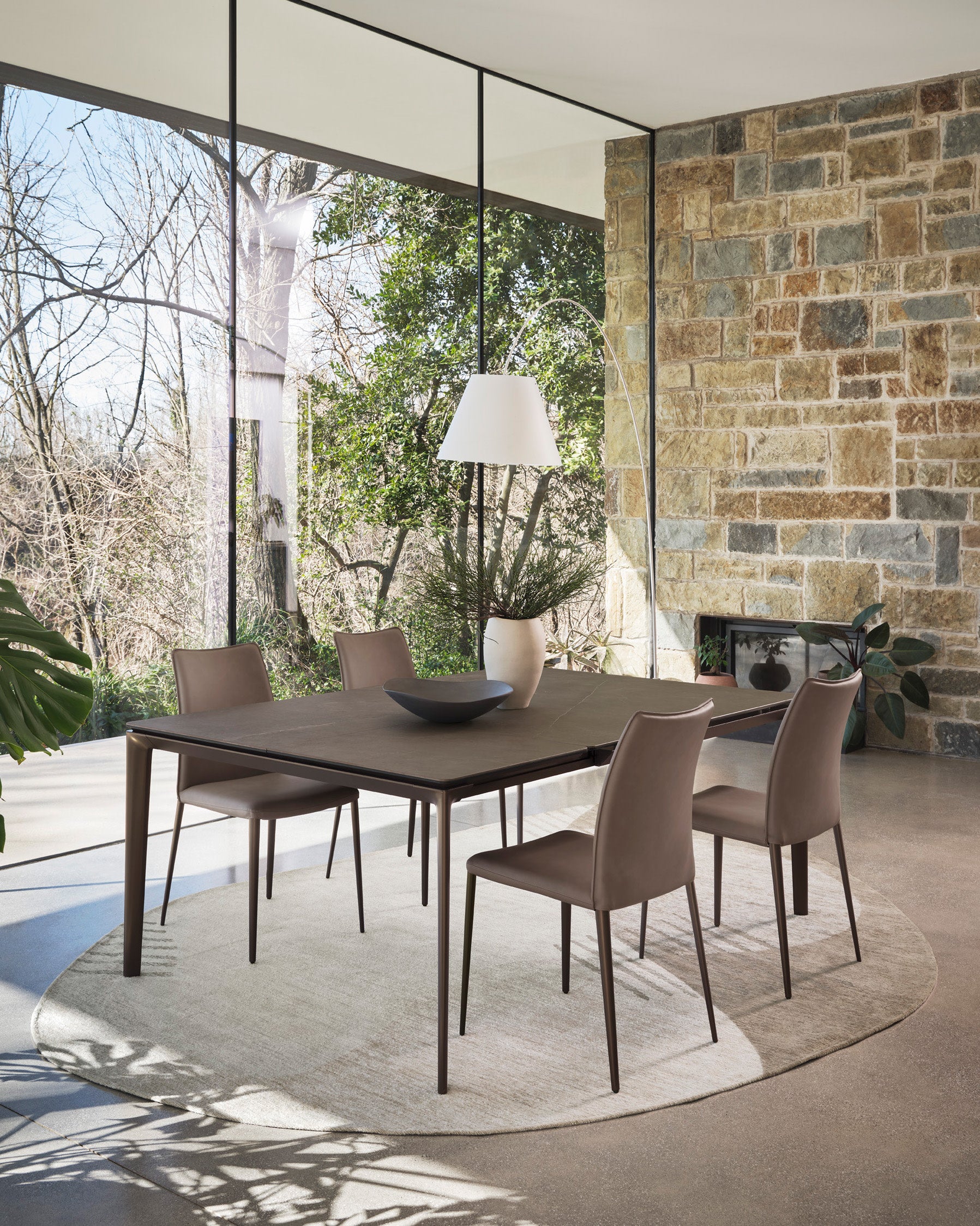 Ombra rug by Calligaris under a dining table in a room with glass walls and a stone wall