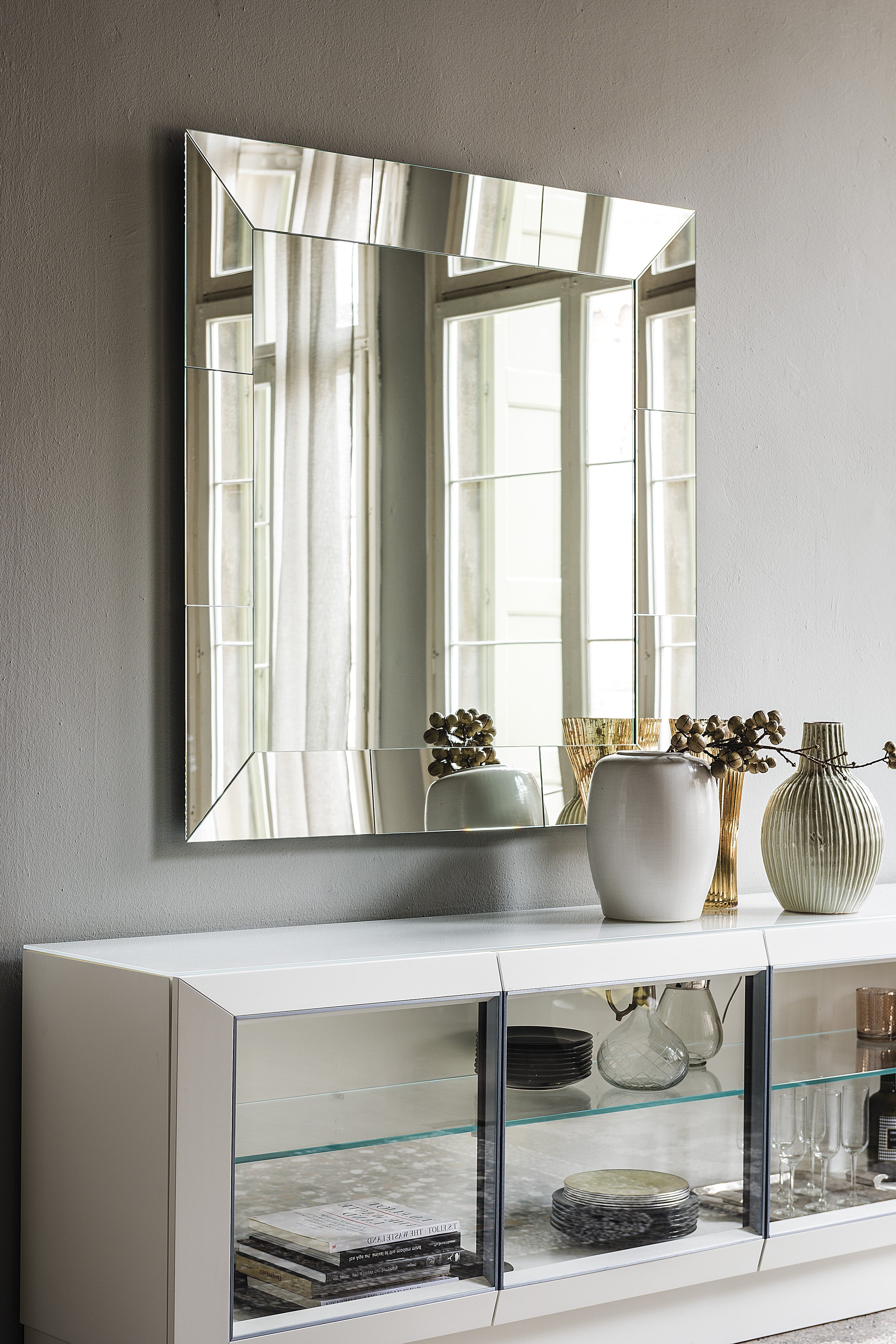 Clear mirrored square Regal mirror above a white glass-front sideboard with vases