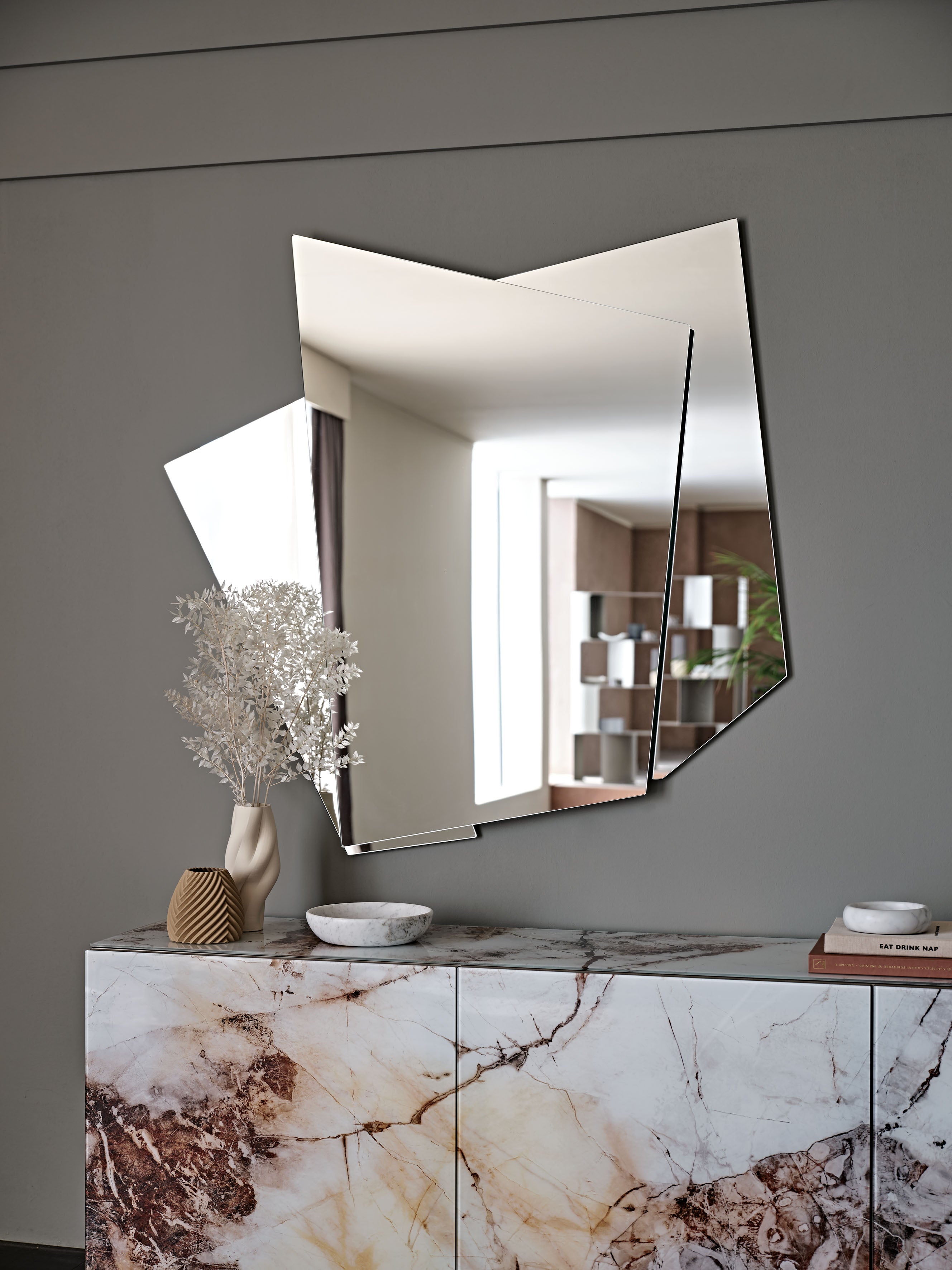 Risiko mirror on a grey wall above a marble-effect sideboard with dried white flowers
