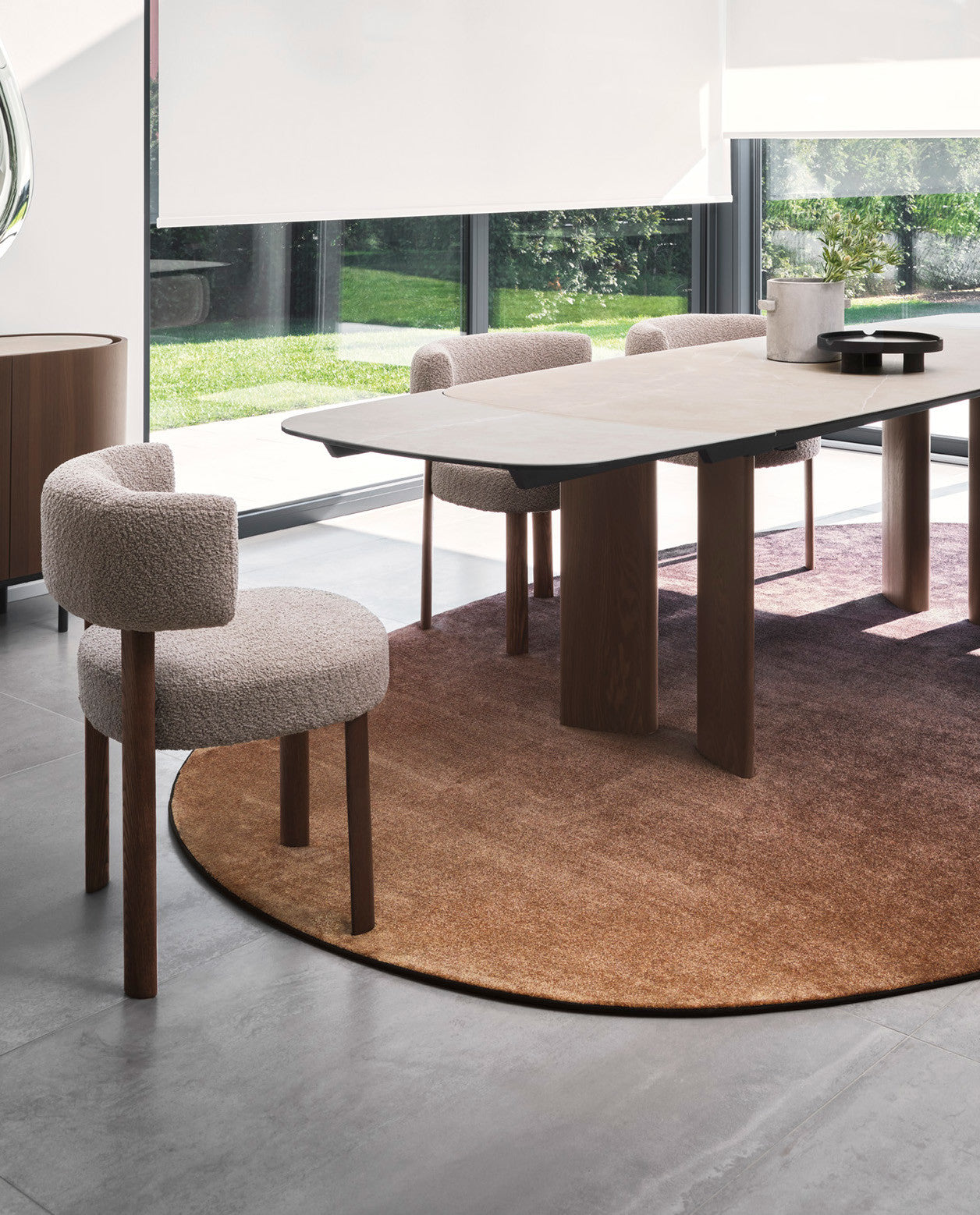 Sky oval rug by Calligaris under a dining table, with a textured upholstered chair and a wood sideboard