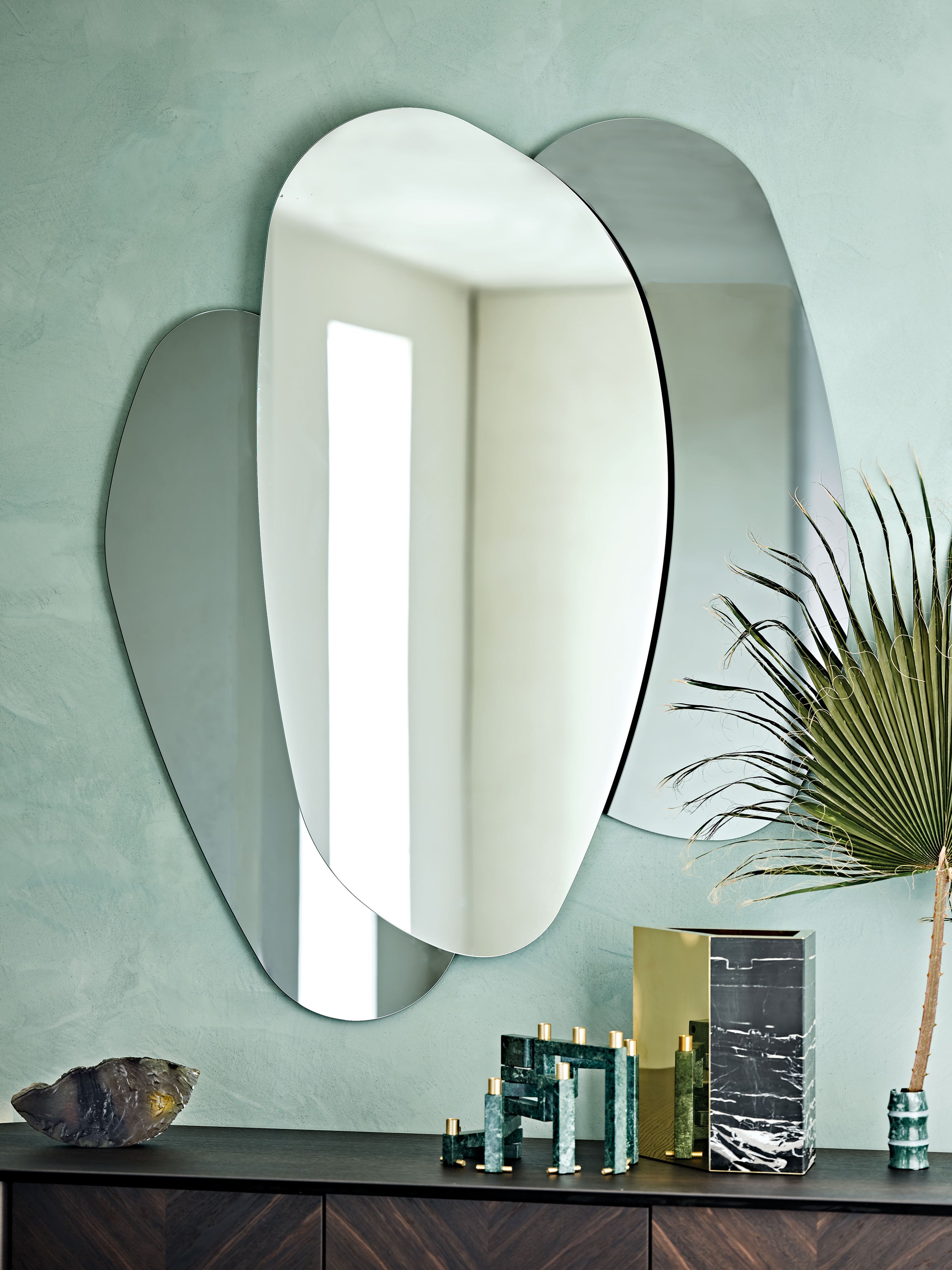 Ulisse mirror on a sage-green plaster wall above a dark wood sideboard